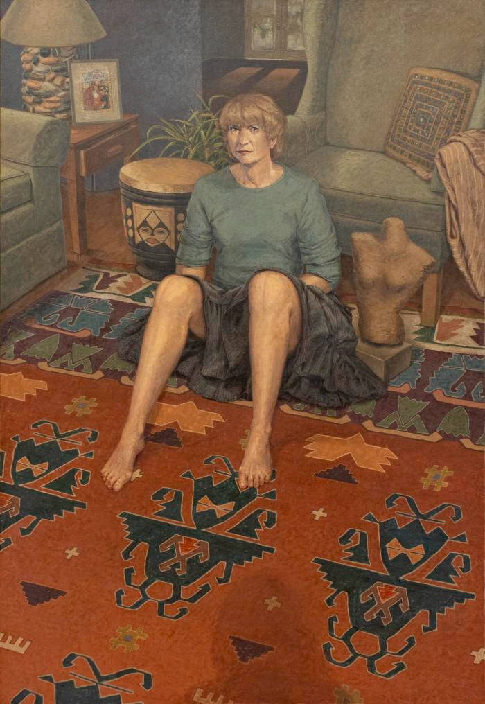 Image of woman sitting against a green chair in blue skirt and dark blond hair, with both knees up.